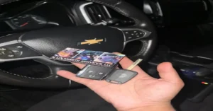 Hand holding car keys and a locksmith's business card near the steering wheel of a Chevrolet. Tips to avoid automotive locksmith scams and ensure reliable, professional service