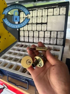 A hand holding a lock cylinder and key, with a display case of Kwikset and Schlage cylinders in the background, showcasing the residential locksmith services offered by A1 Locksmith Services, LLC