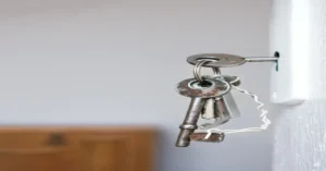 Close-up of old metal keys hanging in a white door lock, showing signs of rust and wear, symbolizing outdated or vulnerable home security.