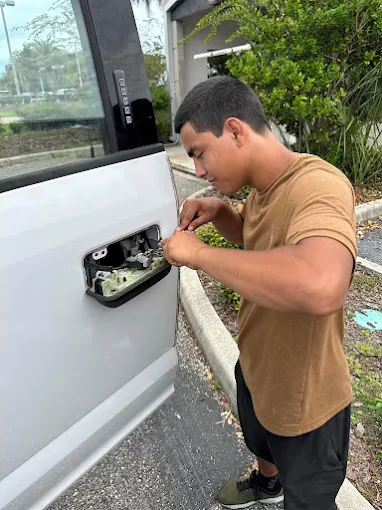 A locksmith from A1 Locksmith Services LLC works on a vehicle door lock, performing a professional car key replacement service in an outdoor parking area.
