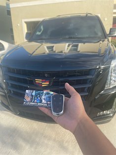 A1 Locksmith Services LLC technician holds a new car key fob and business card in front of a black Cadillac SUV, representing expert car key replacement service.