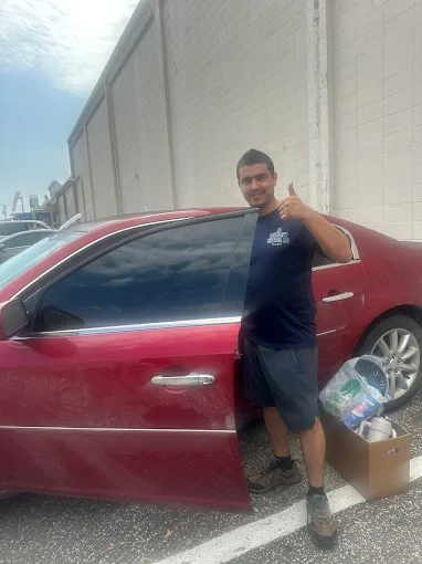 A locksmith from A1 Locksmith Services LLC stands beside a red car giving a thumbs up after completing a successful broken key extraction service.