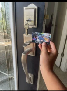 A hand holding an A1 Locksmith Services business card in front of a door lock with a Baldwin brand key inserted into the lock. The door has a modern brushed nickel handle and lock set.